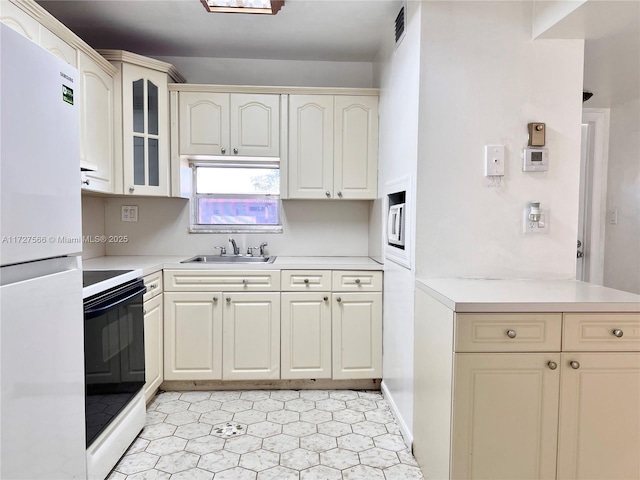 kitchen featuring sink, cream cabinets, and white appliances