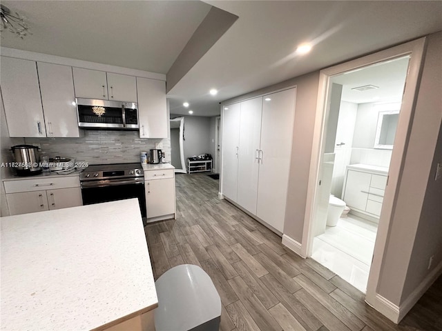 kitchen with white cabinets, light wood-type flooring, appliances with stainless steel finishes, and decorative backsplash