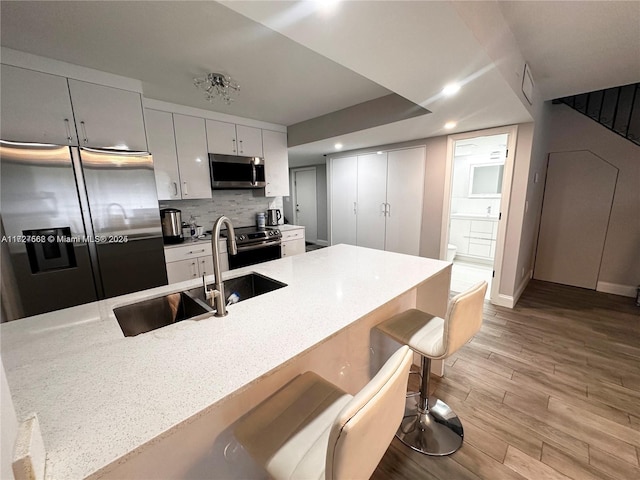 kitchen featuring appliances with stainless steel finishes, white cabinetry, sink, light wood-type flooring, and a breakfast bar