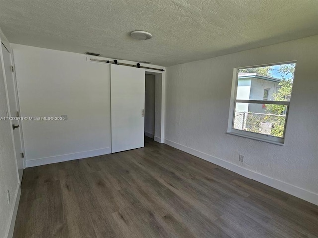 unfurnished bedroom featuring multiple windows, a textured ceiling, dark hardwood / wood-style floors, and a barn door