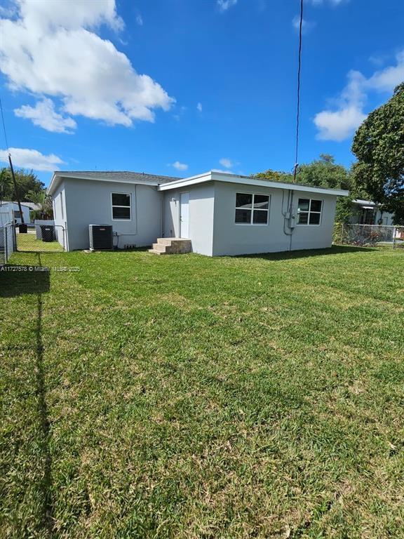 rear view of house featuring central air condition unit and a yard