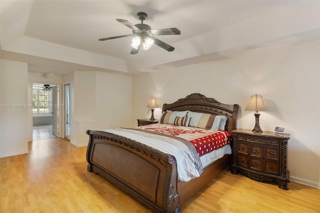 bedroom with ceiling fan, ensuite bath, light hardwood / wood-style flooring, and a raised ceiling