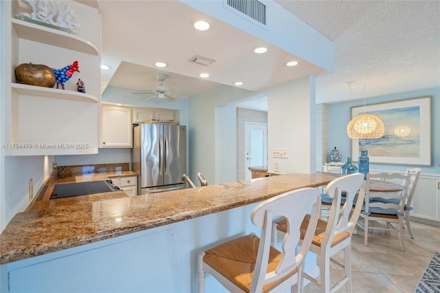 kitchen with white cabinets, hanging light fixtures, stainless steel fridge, kitchen peninsula, and ceiling fan