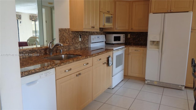 kitchen featuring light tile patterned floors, white appliances, dark stone countertops, light brown cabinetry, and sink