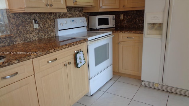 kitchen with white appliances, dark stone counters, light brown cabinetry, backsplash, and light tile patterned floors