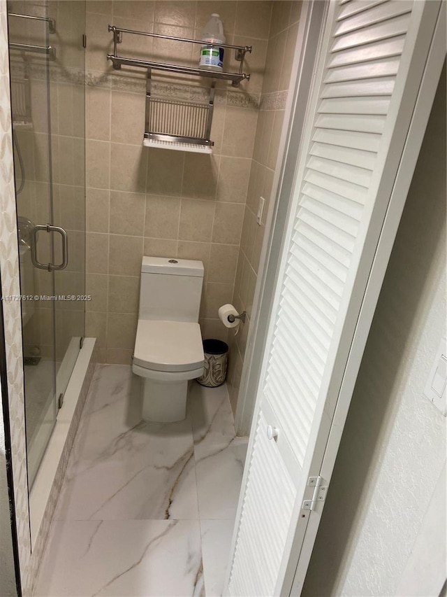 bathroom featuring toilet, a shower with shower door, and tile walls