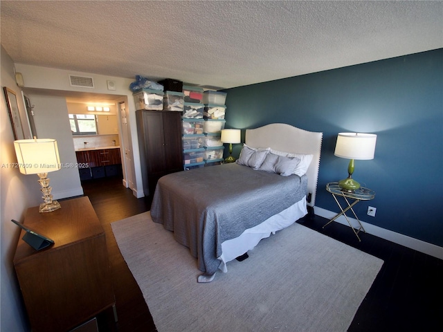 bedroom with ensuite bathroom, dark hardwood / wood-style floors, and a textured ceiling