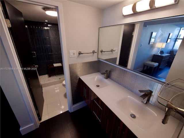 bathroom featuring double vanity, toilet, a stall shower, a sink, and wood finished floors