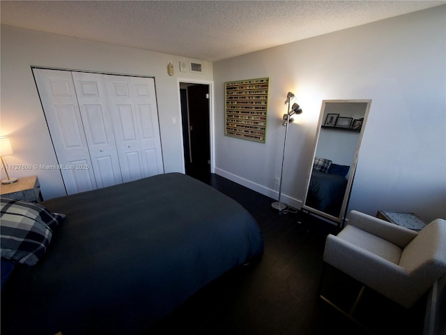 bedroom with a closet, visible vents, dark wood-type flooring, a textured ceiling, and baseboards