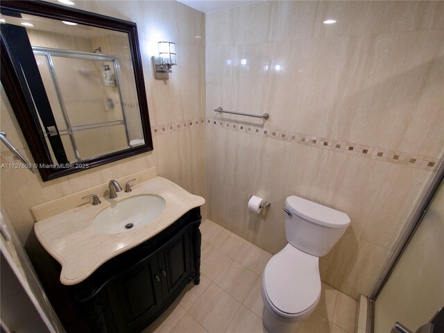 bathroom with tile patterned floors, toilet, a shower with shower door, tile walls, and vanity