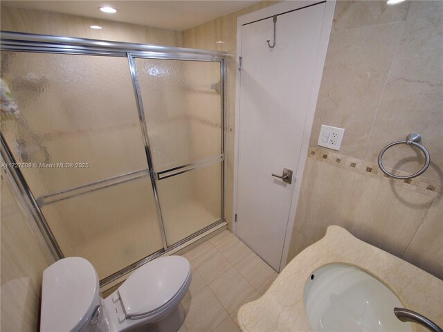 bathroom featuring sink, a shower with door, tile patterned flooring, tile walls, and toilet