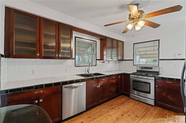 kitchen with tile countertops, tasteful backsplash, sink, stainless steel appliances, and light hardwood / wood-style flooring