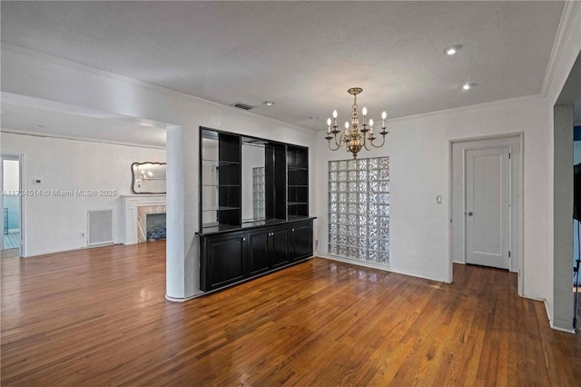 unfurnished dining area featuring a tile fireplace, crown molding, hardwood / wood-style floors, and an inviting chandelier