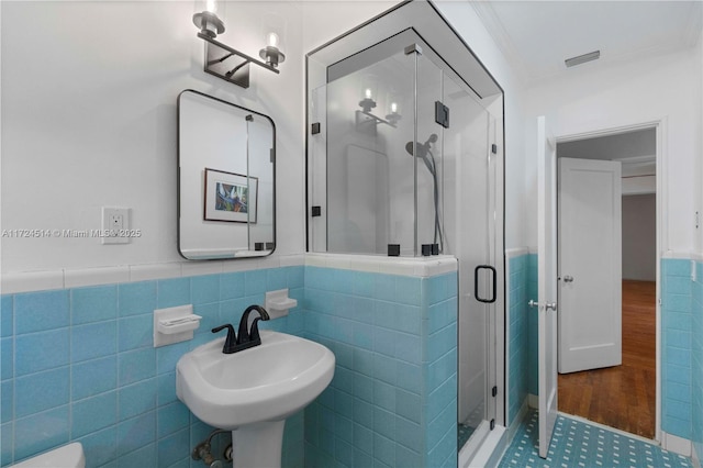 bathroom with a shower with door, crown molding, sink, and tile walls