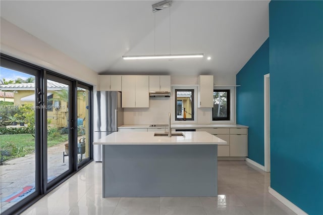 kitchen featuring lofted ceiling, sink, white cabinetry, stainless steel refrigerator, and an island with sink