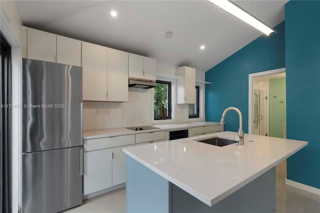 kitchen featuring lofted ceiling, sink, stainless steel fridge, white cabinetry, and an island with sink