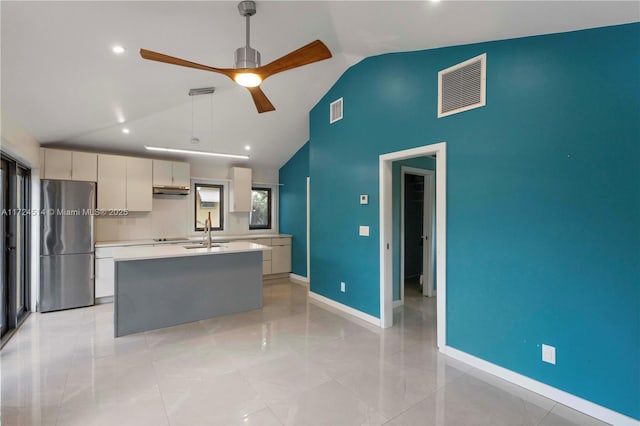 kitchen with sink, stainless steel refrigerator, ceiling fan, hanging light fixtures, and an island with sink