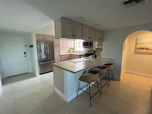 kitchen featuring visible vents, a kitchen breakfast bar, stainless steel appliances, arched walkways, and a peninsula