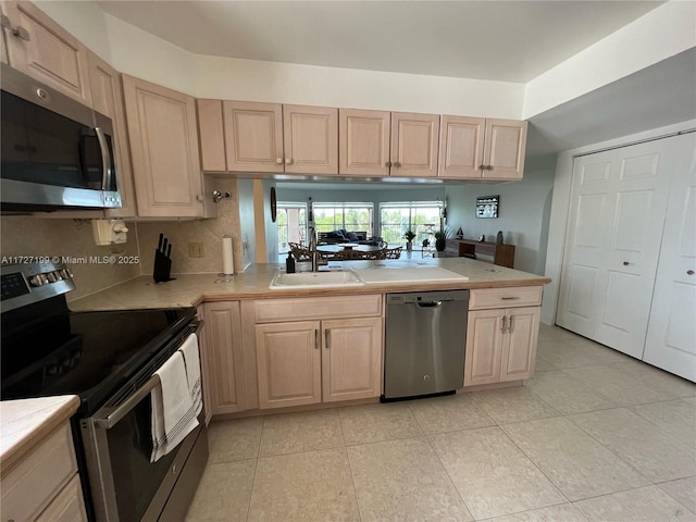 kitchen featuring light brown cabinetry, light countertops, a peninsula, stainless steel appliances, and a sink