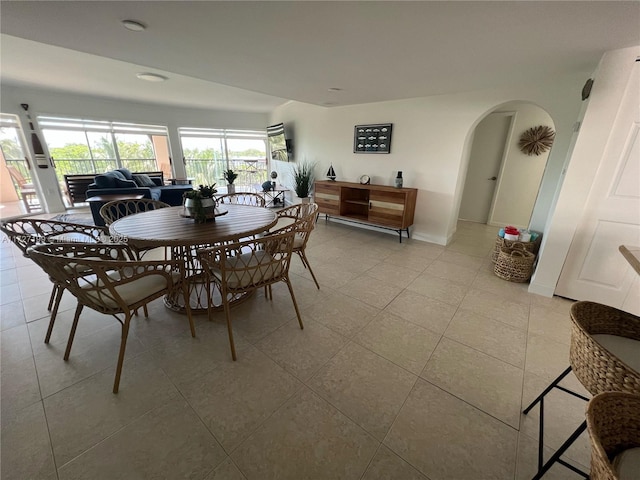 dining area with light tile patterned floors, arched walkways, and baseboards