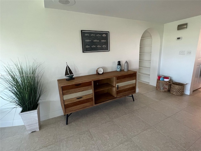 interior space featuring built in features, baseboards, arched walkways, and tile patterned flooring