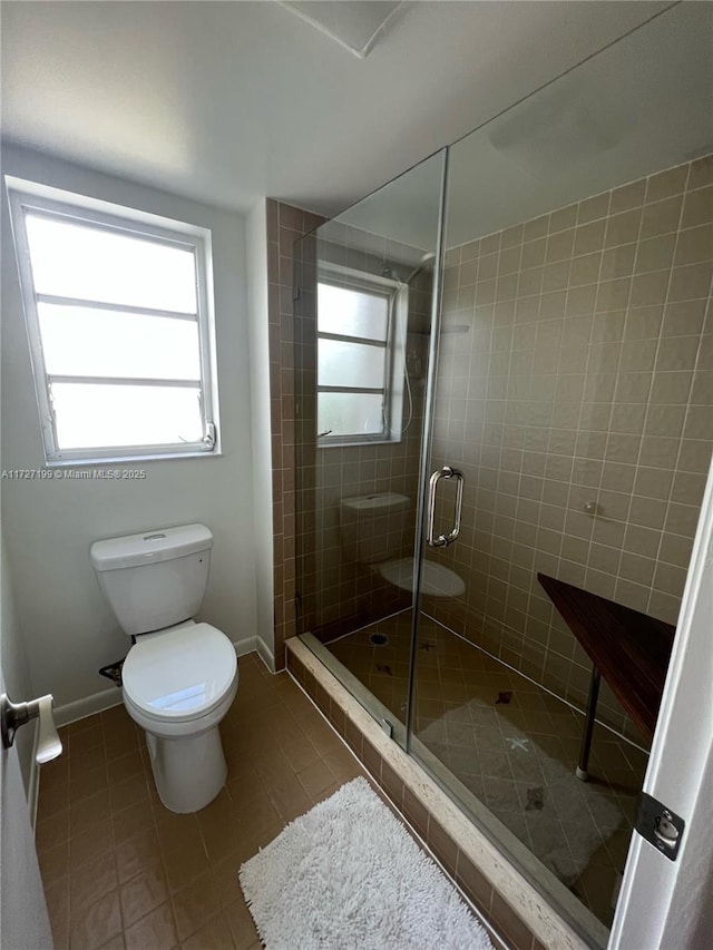 bathroom featuring tile patterned floors, a stall shower, toilet, and baseboards