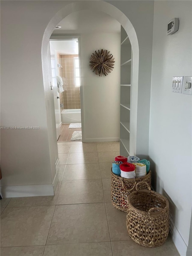 hall with tile patterned floors, baseboards, and arched walkways