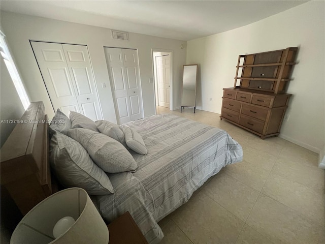 bedroom with light tile patterned floors, visible vents, multiple closets, and baseboards