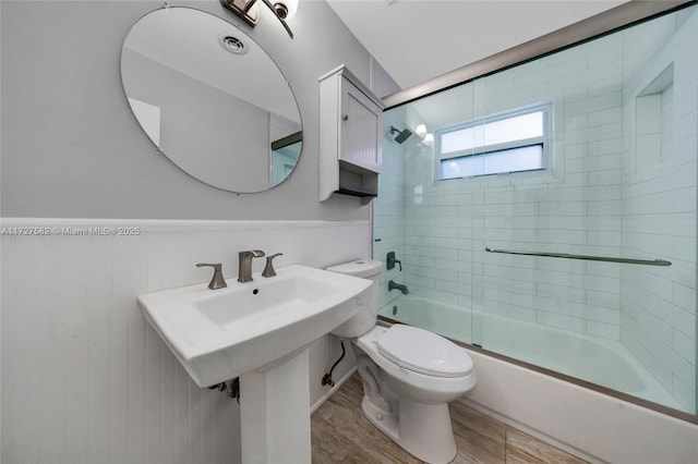 bathroom featuring toilet, wood walls, enclosed tub / shower combo, and wood-type flooring