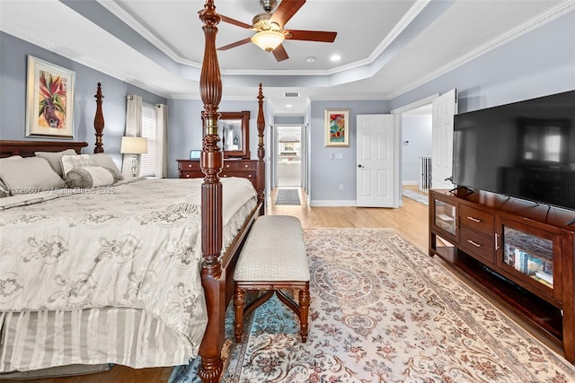 bedroom featuring light wood finished floors, baseboards, a ceiling fan, a tray ceiling, and crown molding