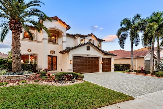 mediterranean / spanish home with a garage, a yard, decorative driveway, and stucco siding