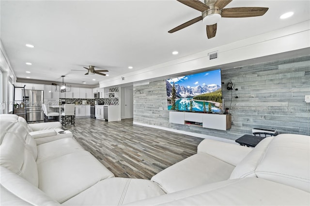 living room featuring wood-type flooring, wooden walls, and ceiling fan