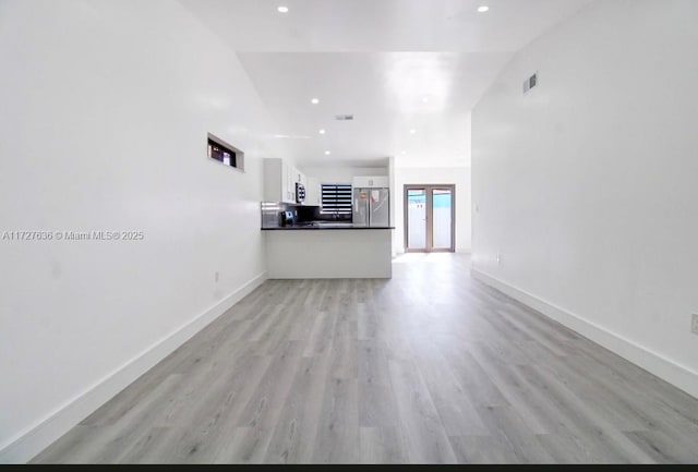 unfurnished living room with vaulted ceiling, french doors, and light wood-type flooring