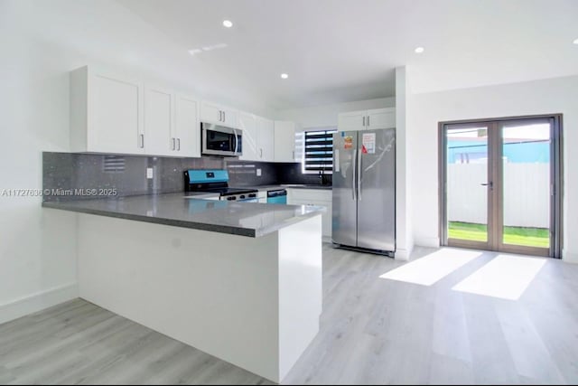 kitchen with white cabinetry, stainless steel appliances, light hardwood / wood-style floors, decorative backsplash, and kitchen peninsula