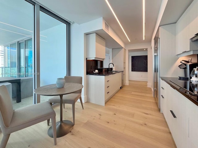 kitchen featuring sink, tasteful backsplash, white cabinets, black electric cooktop, and light wood-type flooring