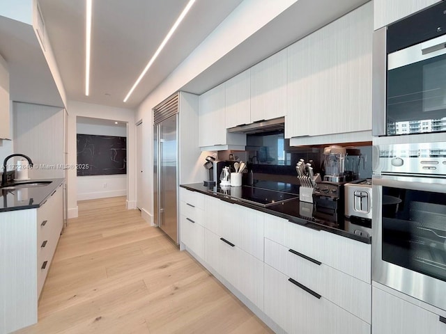 kitchen featuring appliances with stainless steel finishes, sink, white cabinets, and light wood-type flooring