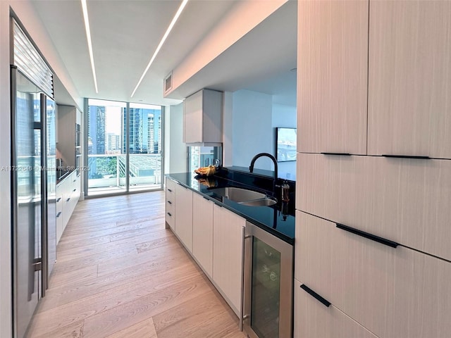 kitchen with sink, high end refrigerator, beverage cooler, expansive windows, and light hardwood / wood-style floors