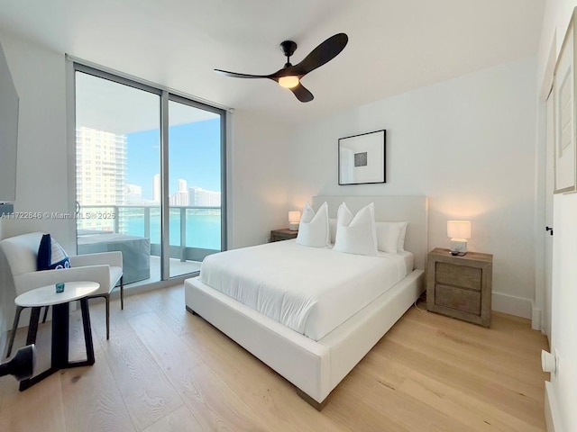 bedroom featuring a wall of windows, ceiling fan, access to exterior, a water view, and light wood-type flooring