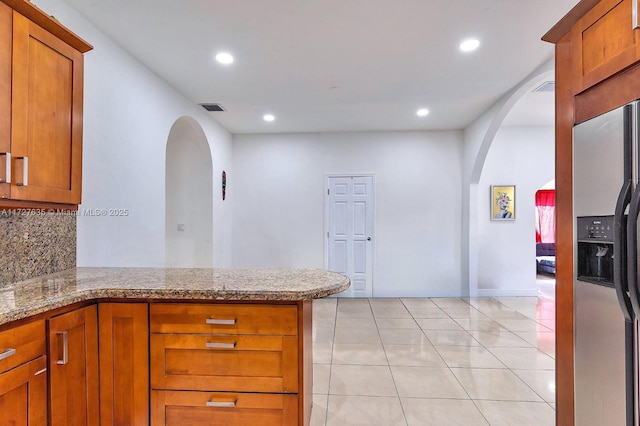 kitchen with arched walkways, a peninsula, visible vents, brown cabinets, and stainless steel fridge