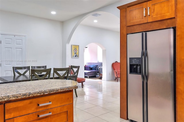 kitchen featuring arched walkways, brown cabinets, light tile patterned floors, visible vents, and stainless steel fridge