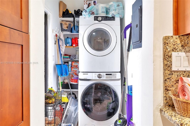 clothes washing area featuring stacked washing maching and dryer, electric panel, and laundry area