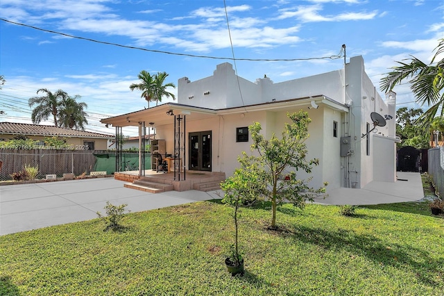 back of house with stucco siding, a patio, a lawn, and fence