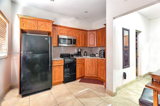 kitchen featuring light tile patterned floors, tasteful backsplash, brown cabinetry, black appliances, and a sink