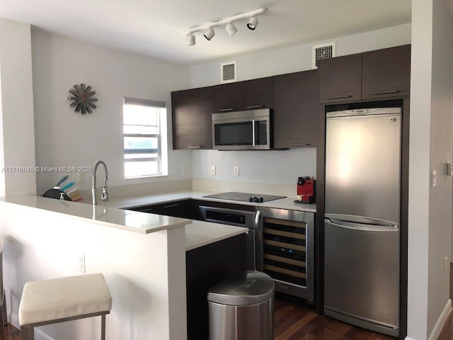 kitchen with a kitchen bar, stainless steel appliances, wine cooler, sink, and kitchen peninsula