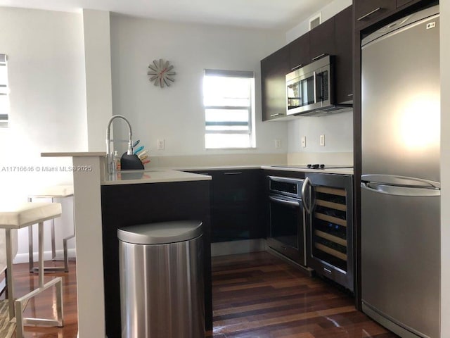 kitchen with beverage cooler, appliances with stainless steel finishes, dark hardwood / wood-style flooring, sink, and kitchen peninsula