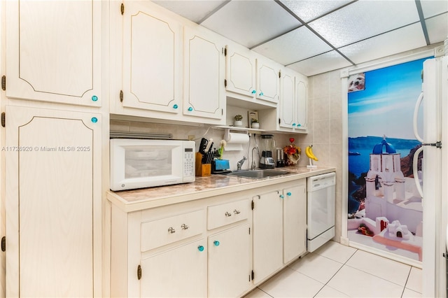 kitchen with light tile patterned floors, white cabinetry, white appliances, a drop ceiling, and sink