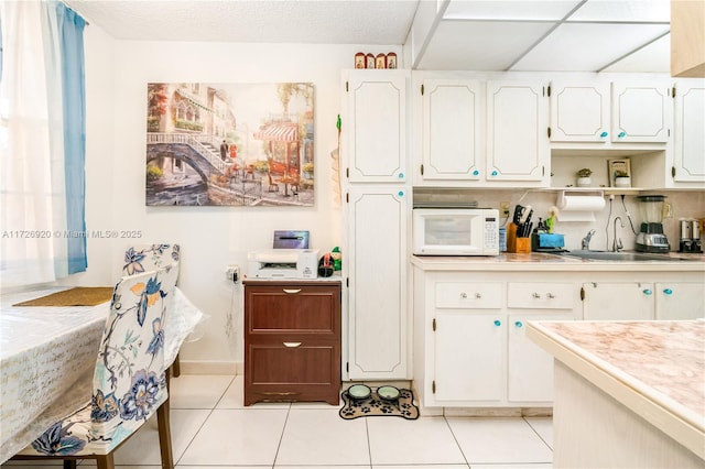 kitchen with light tile patterned floors, a textured ceiling, white cabinets, and sink