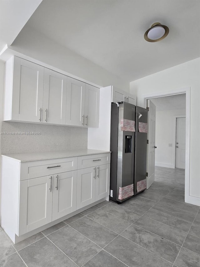 kitchen featuring stainless steel fridge, light tile patterned flooring, and white cabinetry