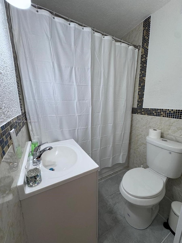 bathroom featuring toilet, vanity, tile walls, tile patterned floors, and a textured ceiling