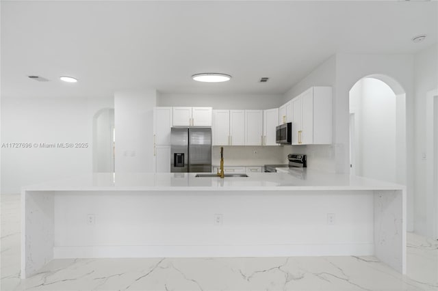 kitchen with kitchen peninsula, sink, stainless steel appliances, and white cabinetry